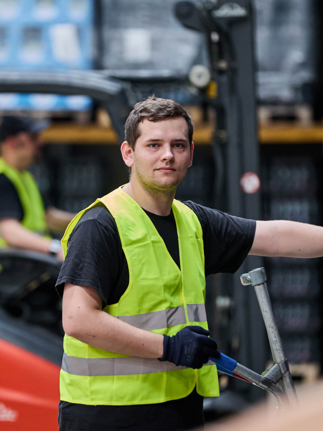 Lagerarbeiter mit Warnweste bedient einen Hubwagen im Getränkelager