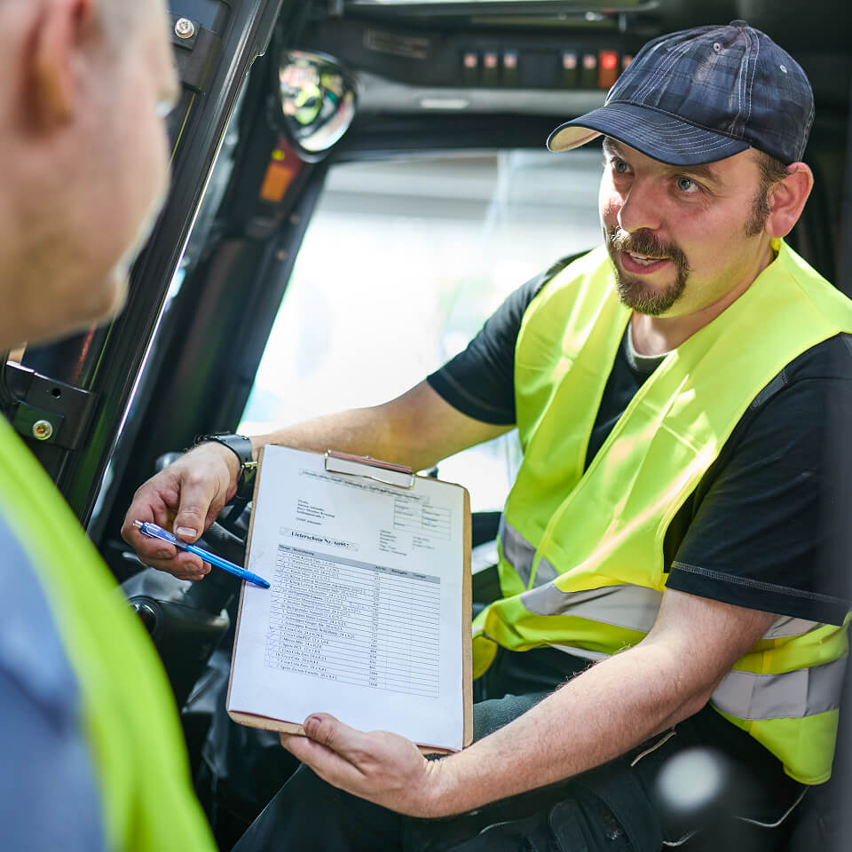 Lagerarbeiter erklärt Kollegen ein Formular im Staplerfahrzeug