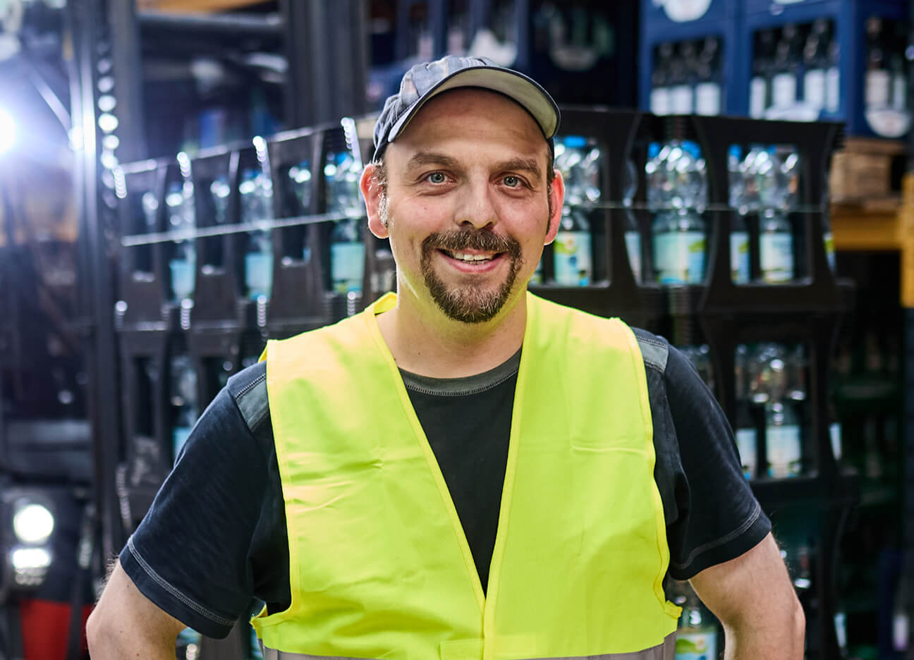 Lagerarbeiter mit Warnweste lächelt in einem Getränkelager