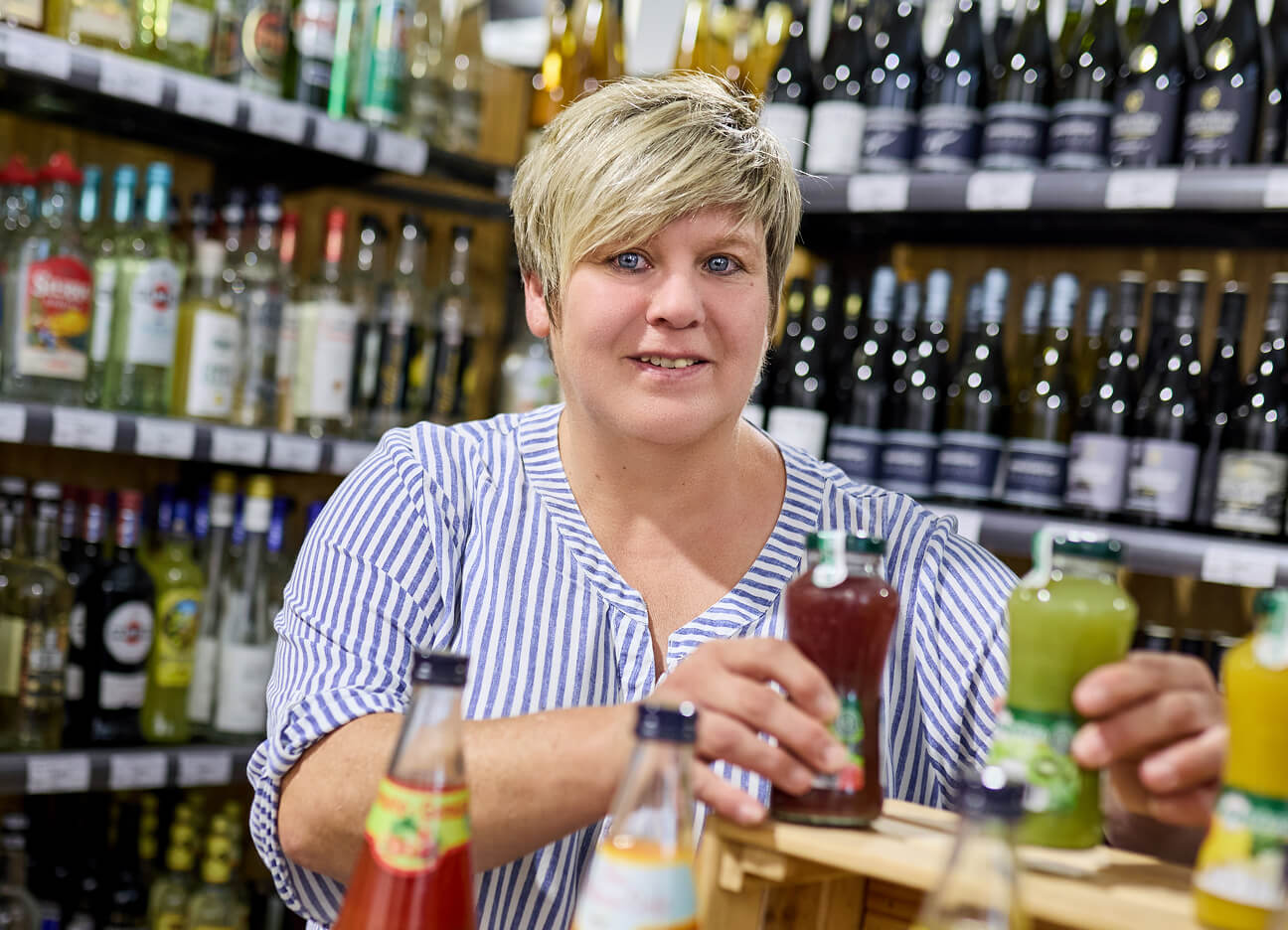 Mitarbeiterin sortiert Saftflaschen im Verkaufsregal