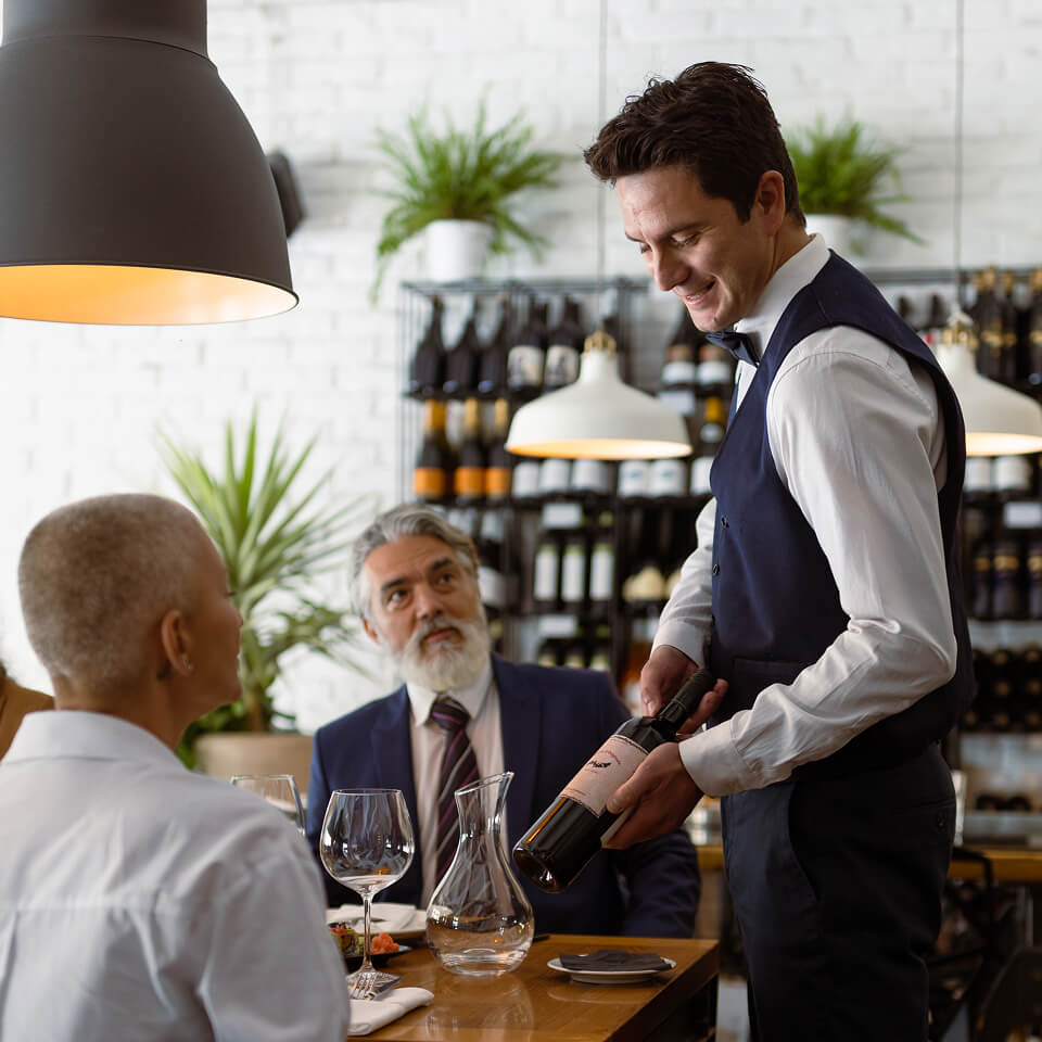 Kellner serviert Wein an zwei Gäste im Restaurant