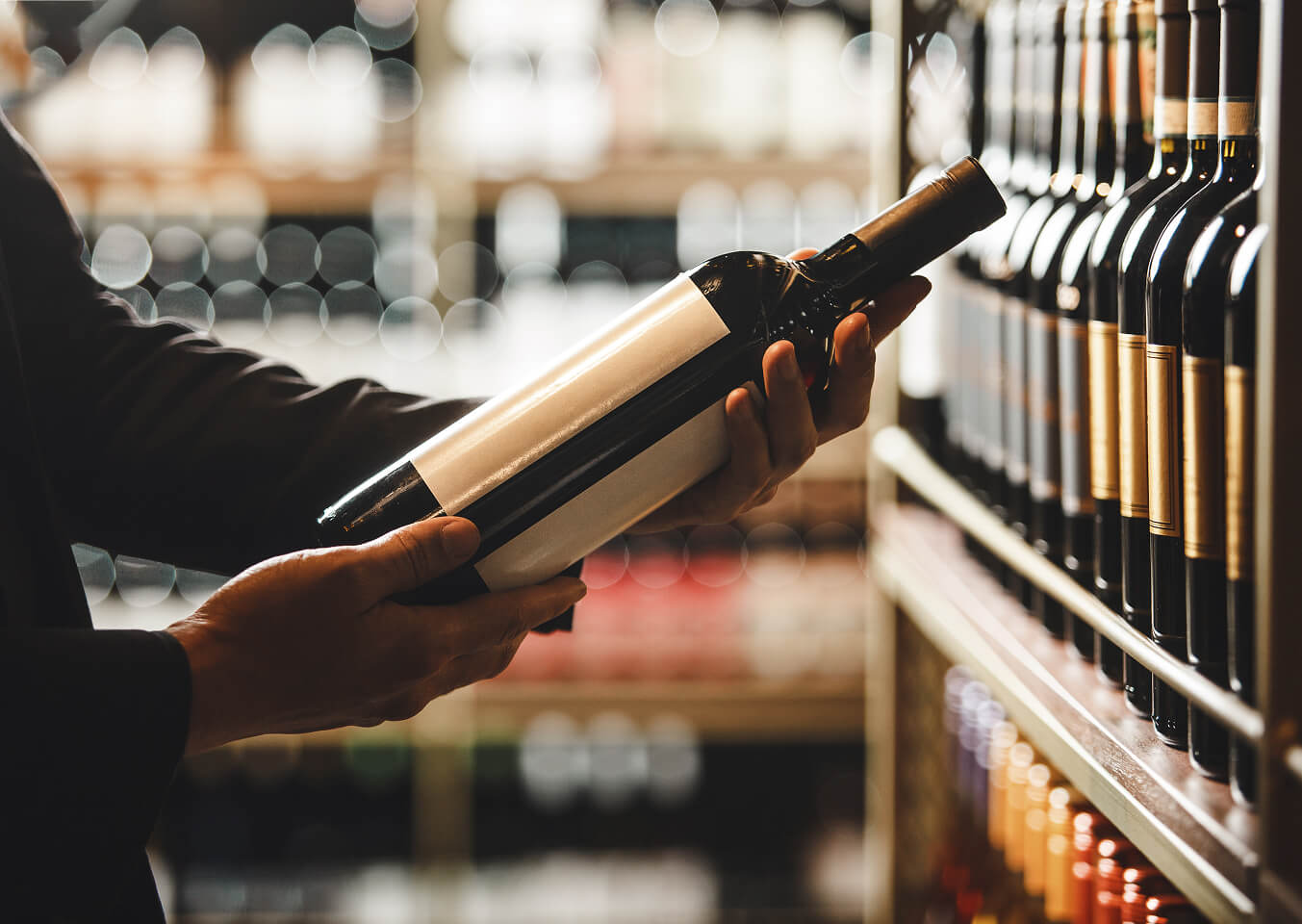 Person betrachtet Weinflasche im Weinregal