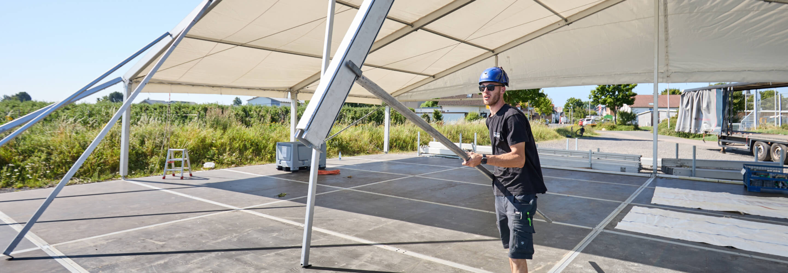 Mitarbeiter montiert Zeltkonstruktion auf einer offenen Fläche