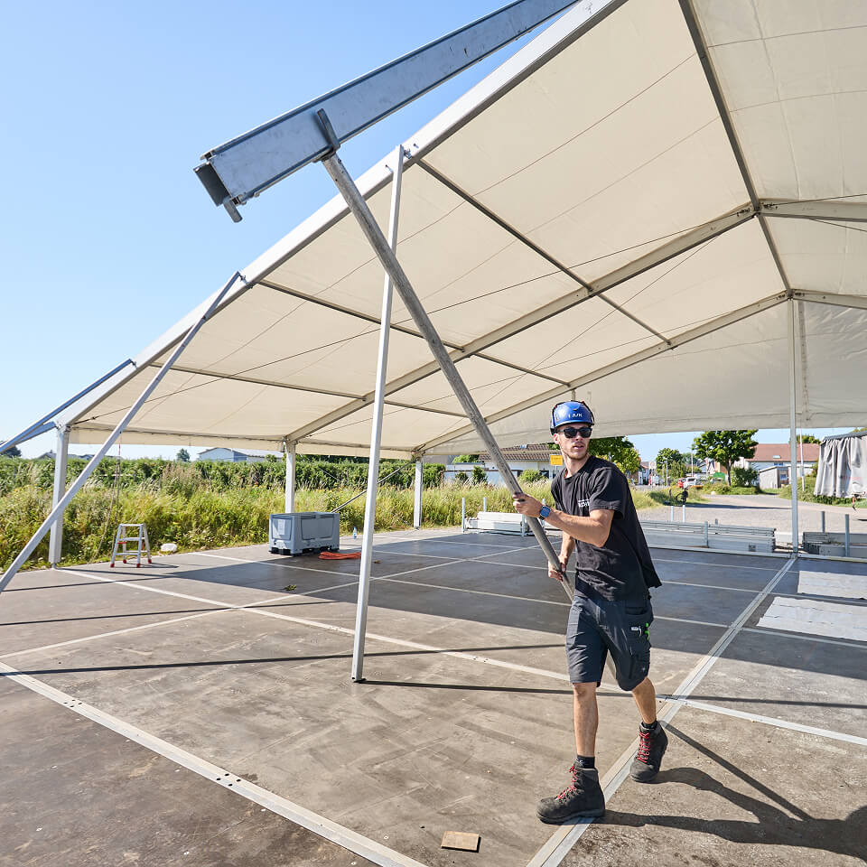 Mitarbeiter richtet ein Zeltgestänge auf einer befestigten Fläche aus